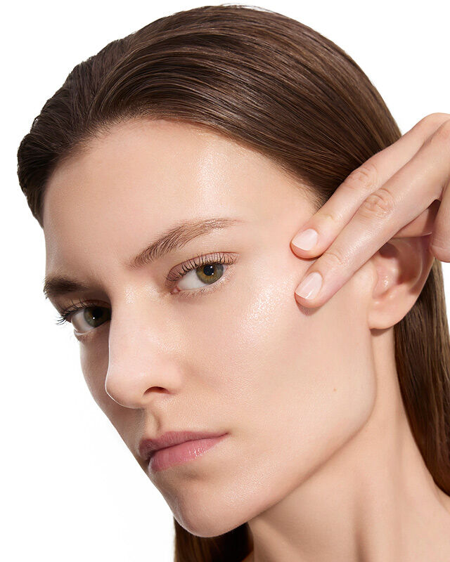 Marije, YSL Beauty-model, met een lichte huid, die voorzichtig haar wang aanraakt en gladde huid toont na het aanbrengen van lotion.