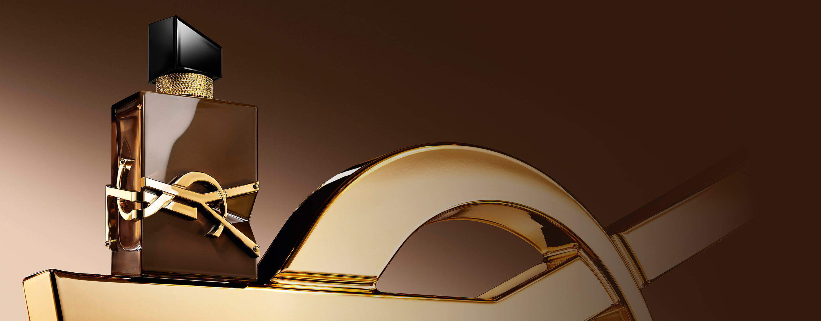 Geglazuurde bruine Libre Santal Couture-fles die licht weerkaatst, geplaatst op een grote gouden YSL Cassandre.