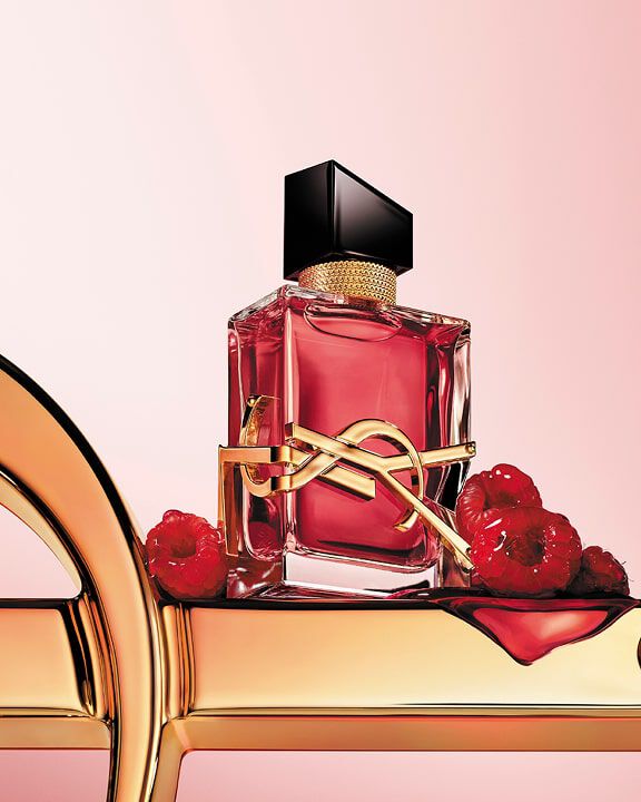 Rode YSL-parfumfles met gouden logo, op een gouden oppervlak met frambozen.